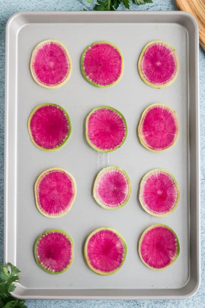 watermelon radishes on a baking sheet about to be roasted into chips
