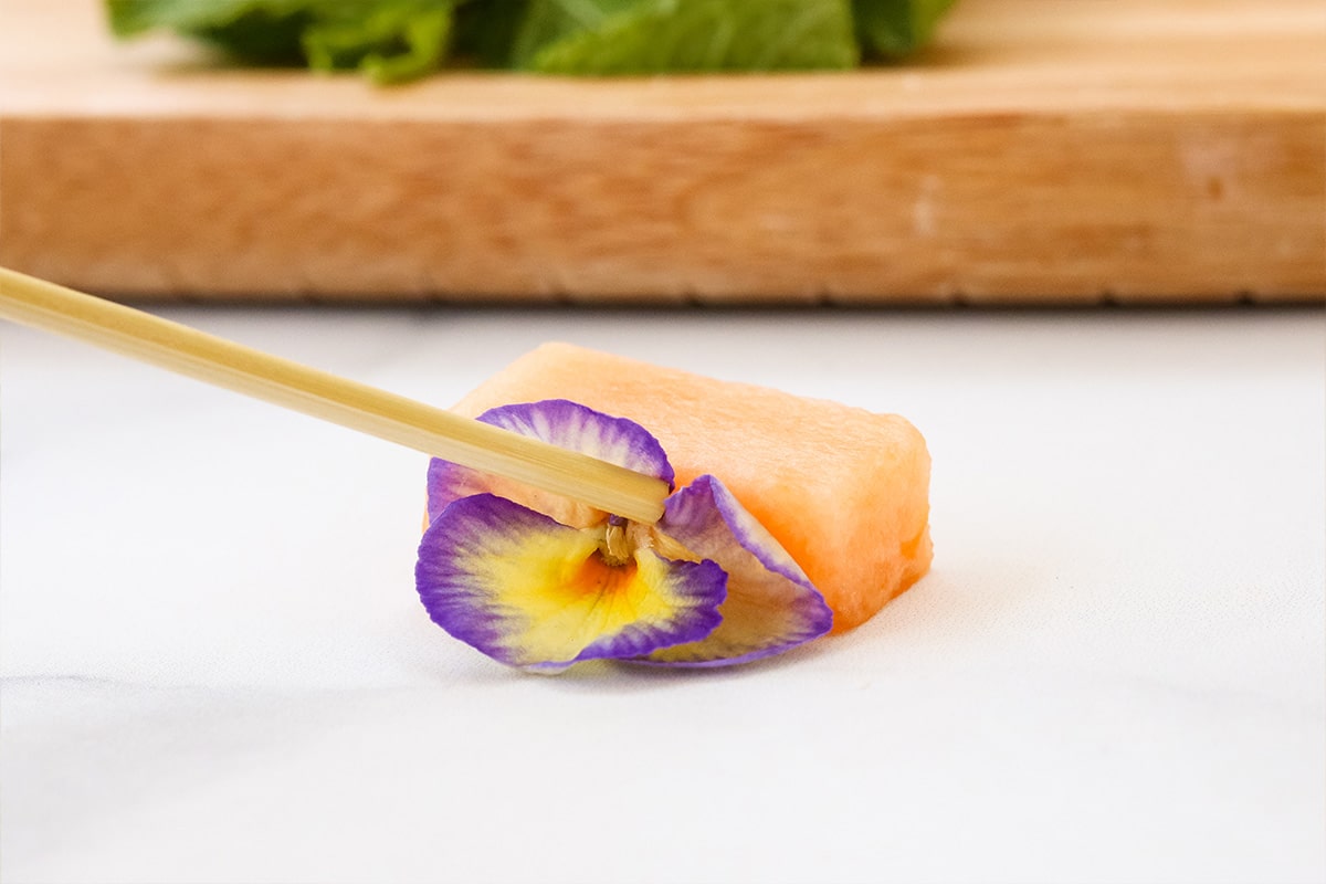 Inserting a flower onto a piece of cantaloupe to make buggy fruit kabob.