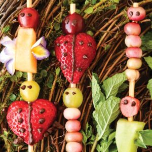 Fruit kabobs in the shape of bugs served on branches with a dip in the middle.
