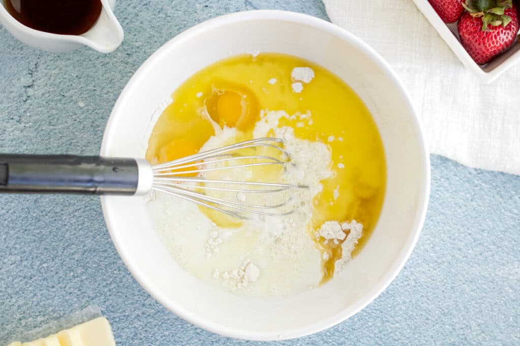 Ingredients for mini pancake cereal being mixed in a white bowl with a blue styling board in the background