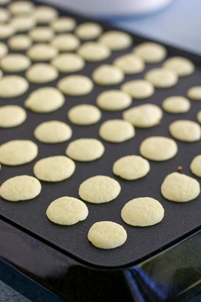 Mini pancakes being cooked on a griddle to make a pancake cereal recipe