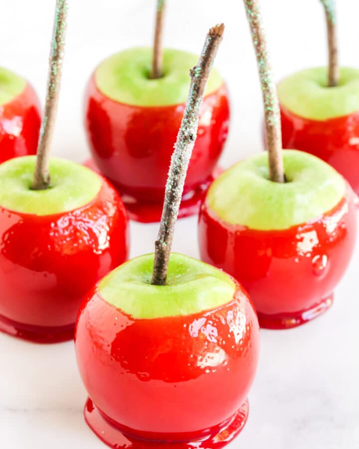 Bright red candy apples on a white marble styling board with glitter topped sticks on top.
