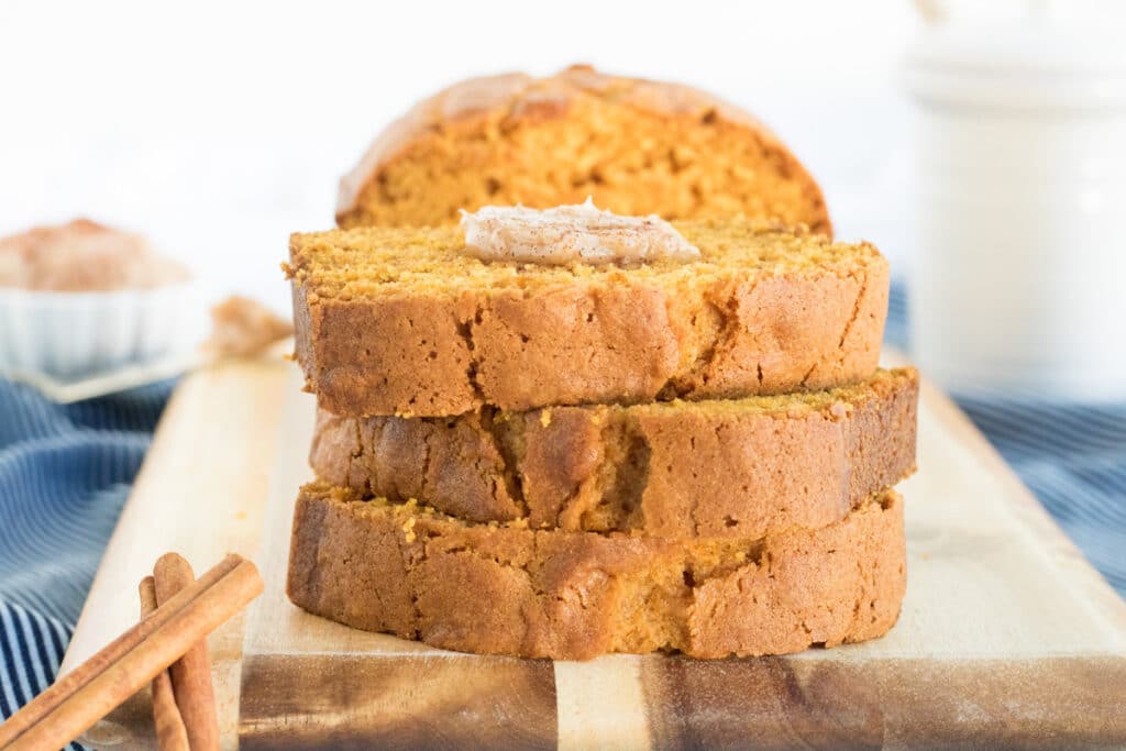 A stack of gluten free pumpkin bread on a cutting board with cinnamon honey butter on top.