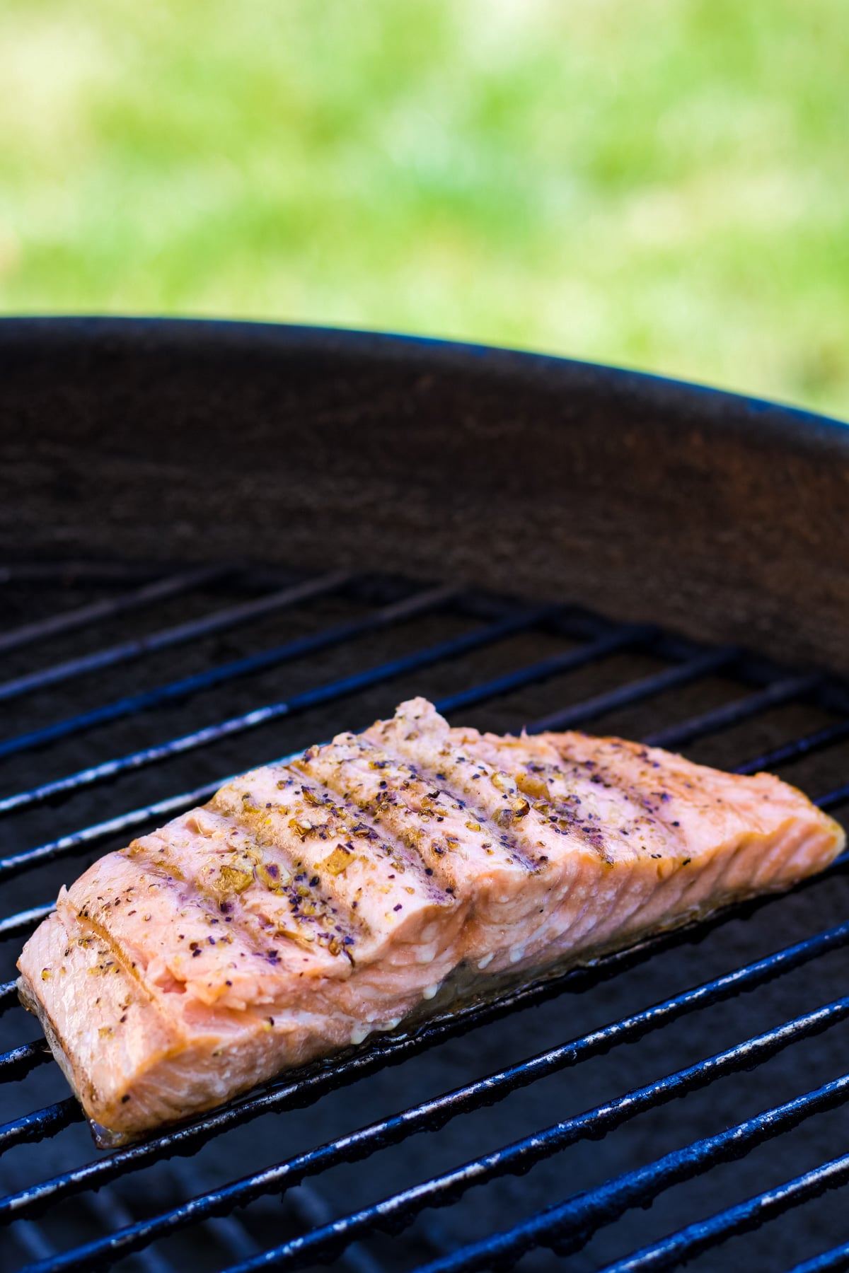 A salmon filet on the grill with seasonings and nice charred grill marks. 