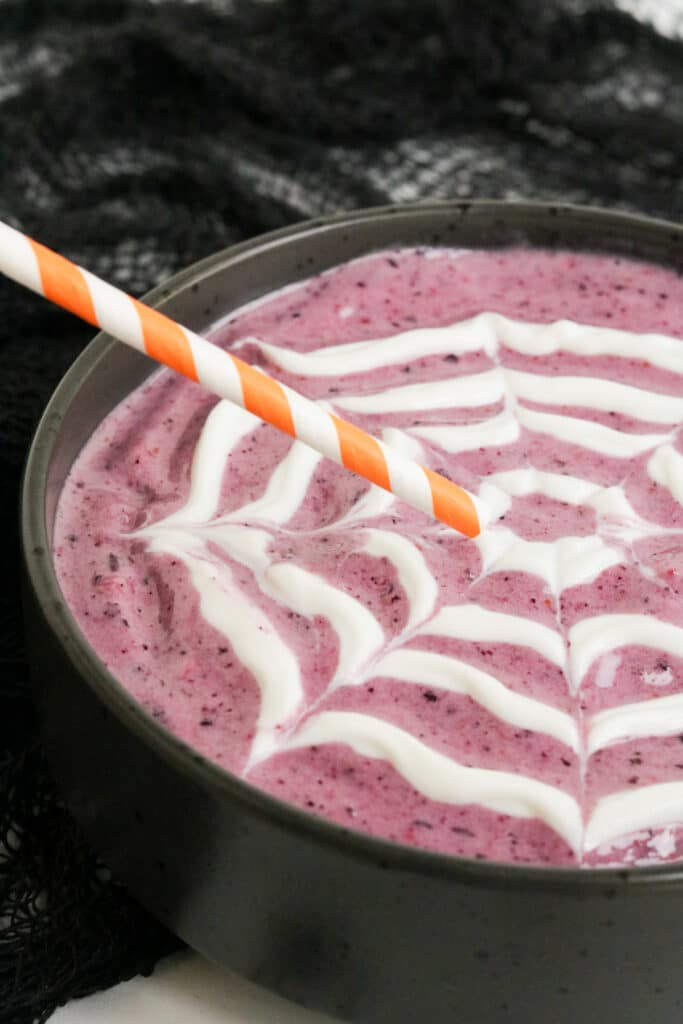 A Halloween Smoothie bowl with a greek yogurt spider web piped on the top.