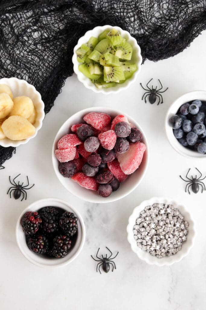 Ingredients to make Halloween Smoothie Bowls - there are little bowls of frozen berries, fresh berries and star sprinkles.