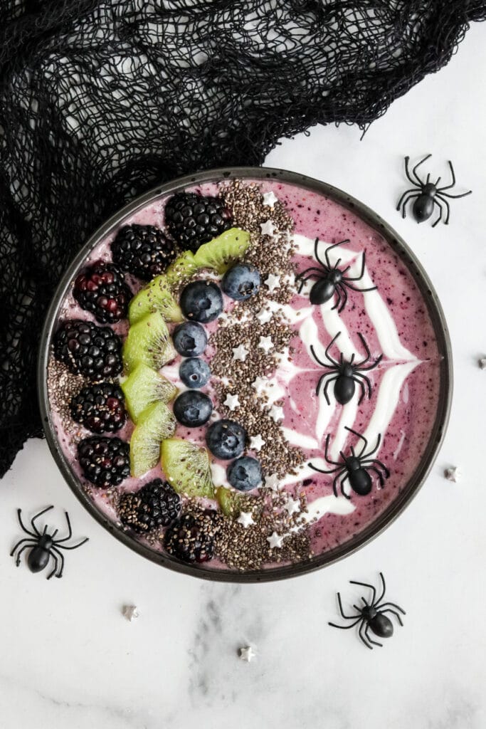 Image of a purple halloween themed smoothie bowl with plastic spiders and a web piped with yogurt