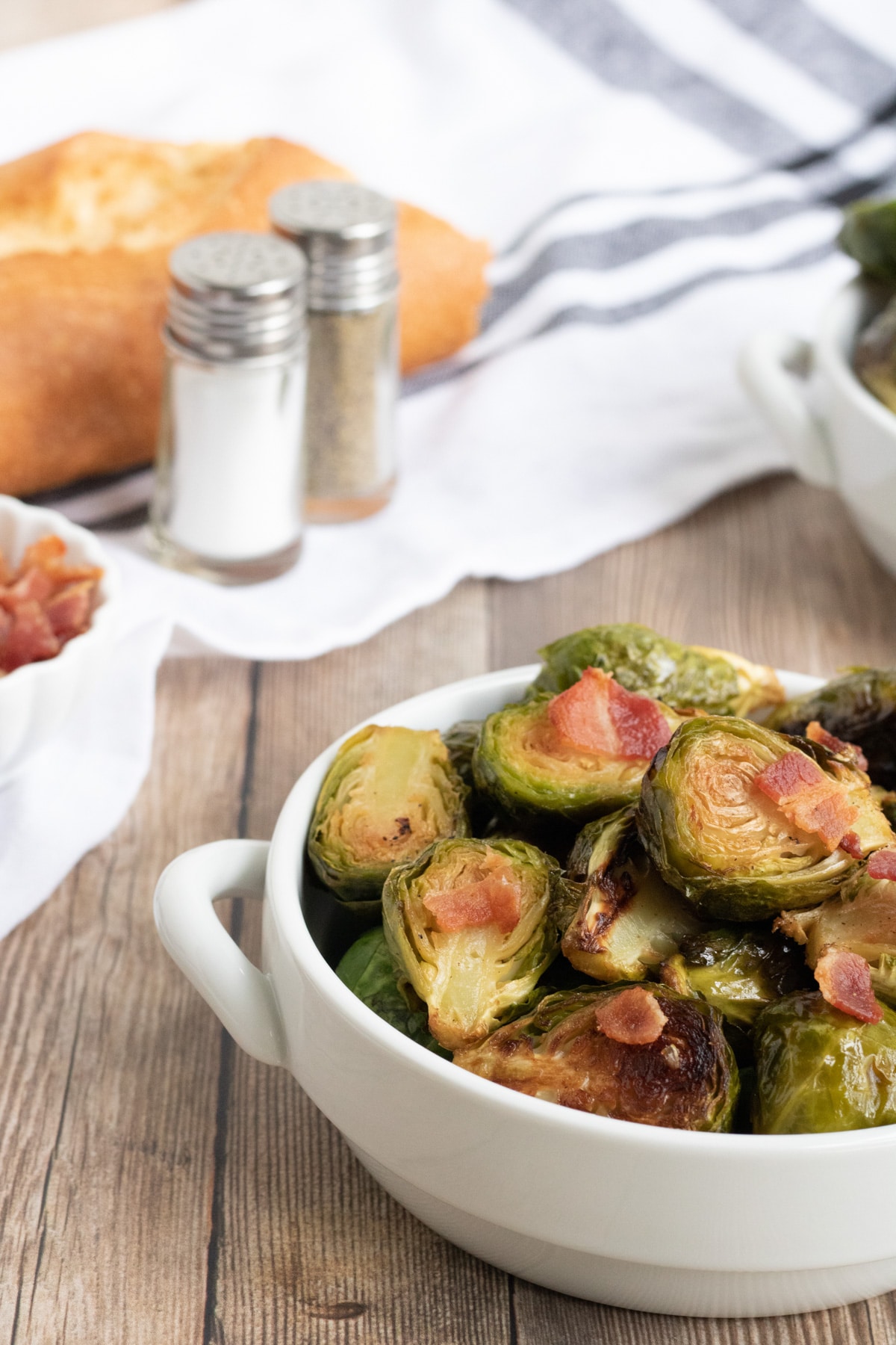 Keto Brussel Sprouts in a white dish on a wooden styling board with bacon on top. 