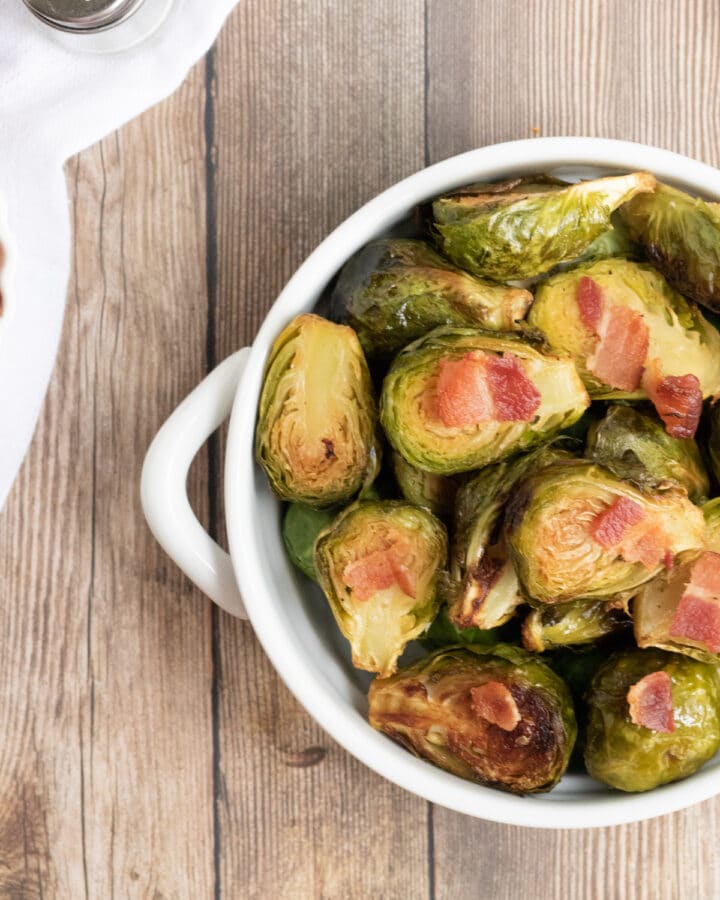 Keto Brussel Sprouts with bacon in a white bowl with a wooden background.