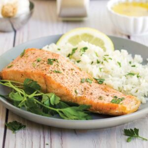 Air fryer salmon with white rice on a grey plate in front of an air fryer.