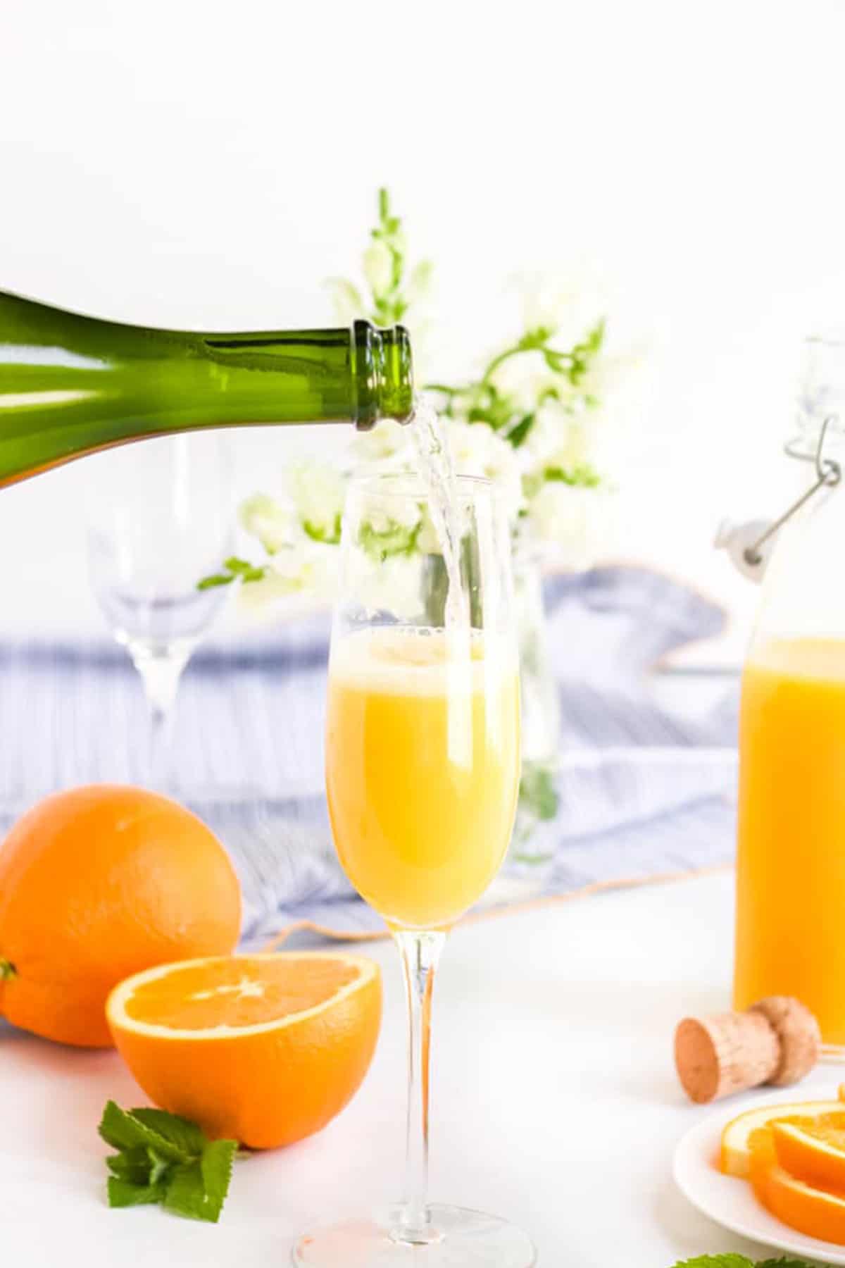 Champagne being poured into a glass of orange juice to make a mimosa. 