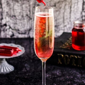 A image of a Halloween Mimosa with a syringe of cherry grenadine.