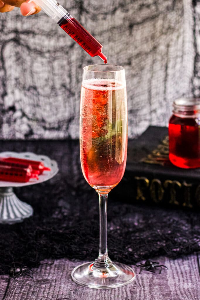 A picture of a syringe of grenadine being dripped into a champagne bottle for Halloween Mimosa