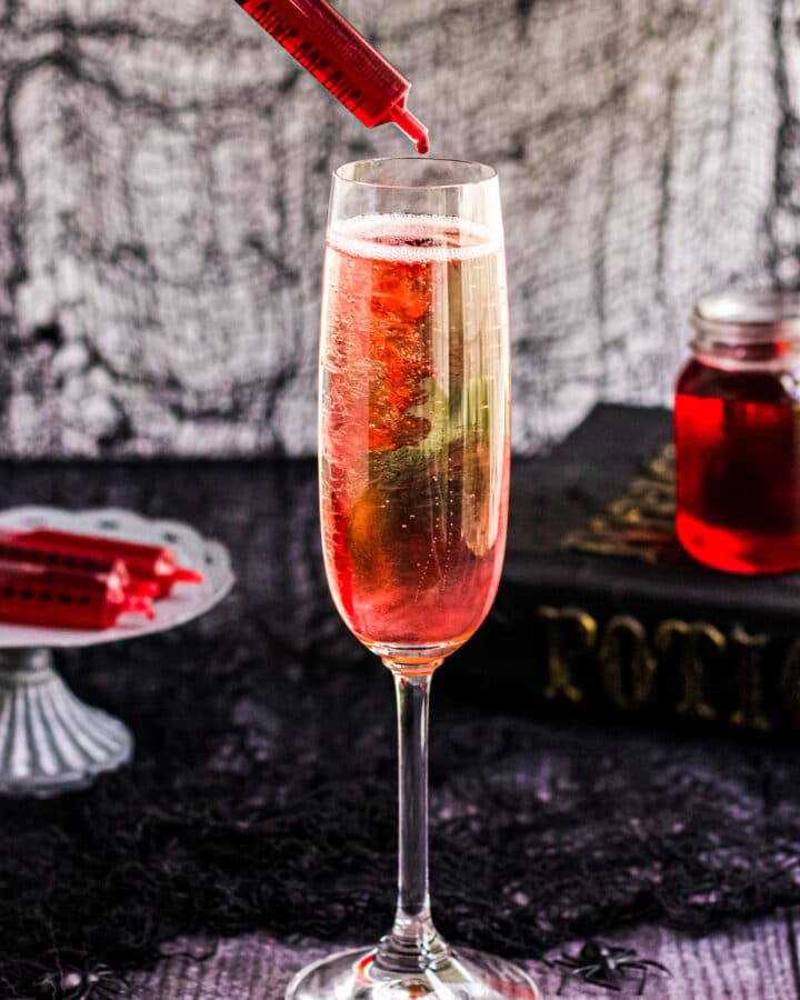 A image of a Halloween Mimosa with a syringe of cherry grenadine.