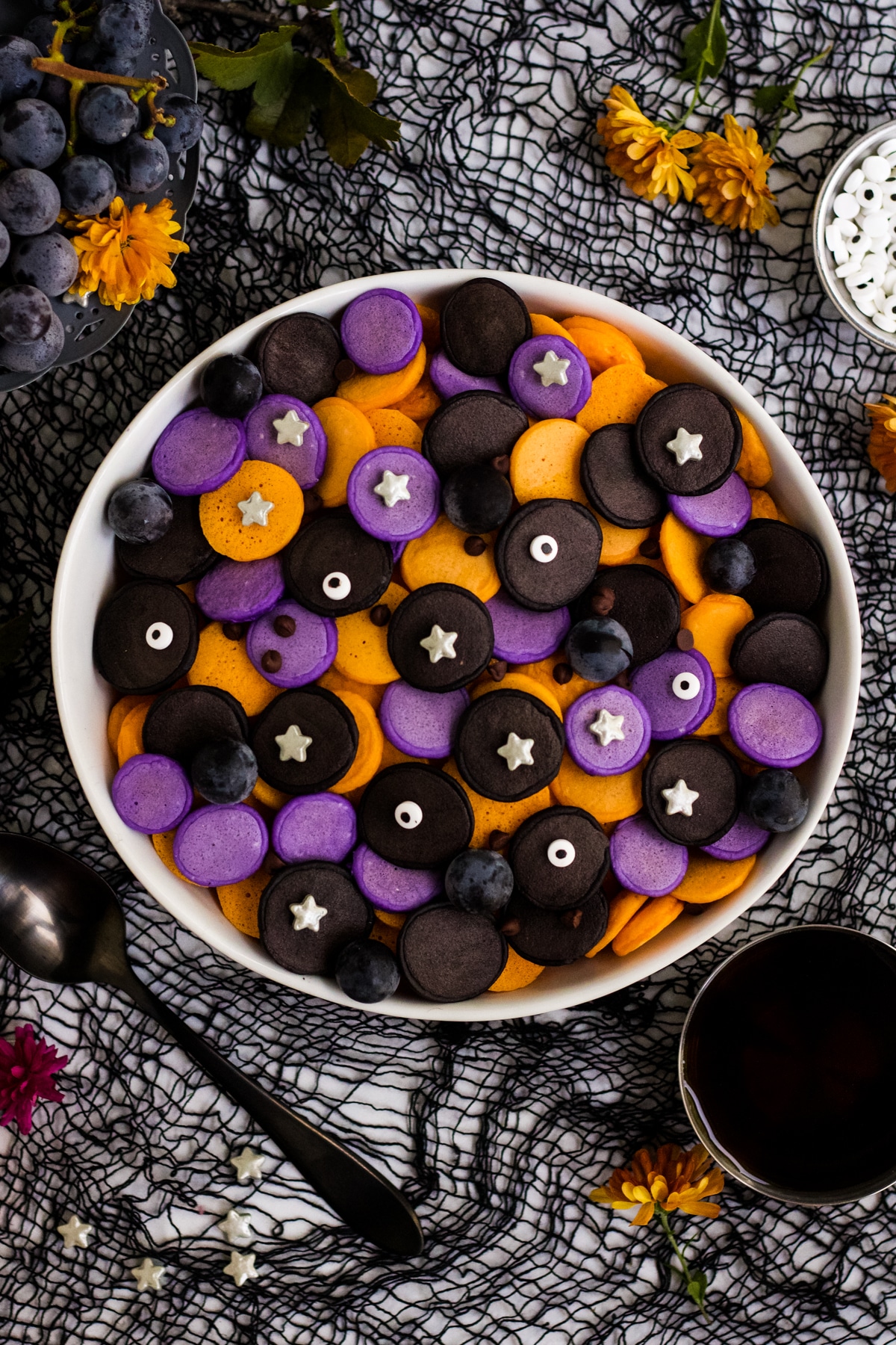A bowl of purple, orange and black mini Halloween pancakes with candy eyes and stars.
