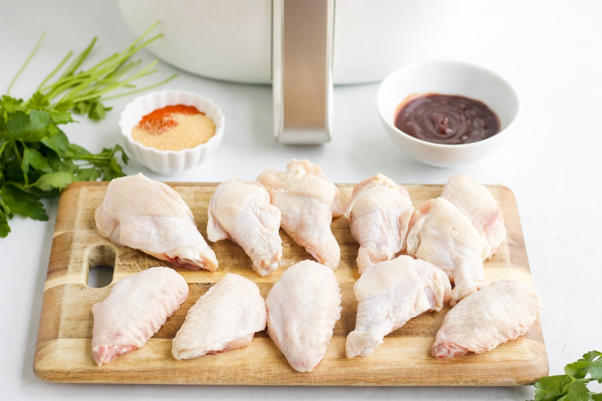Raw chicken wings on a wooden cutting board with other ingredients for air fryer bbq wings.