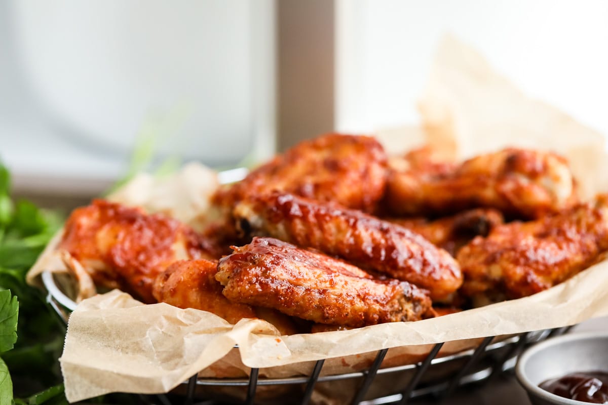 Air fryer bbq chicken wings in a basket with barbecue sauce on the side.