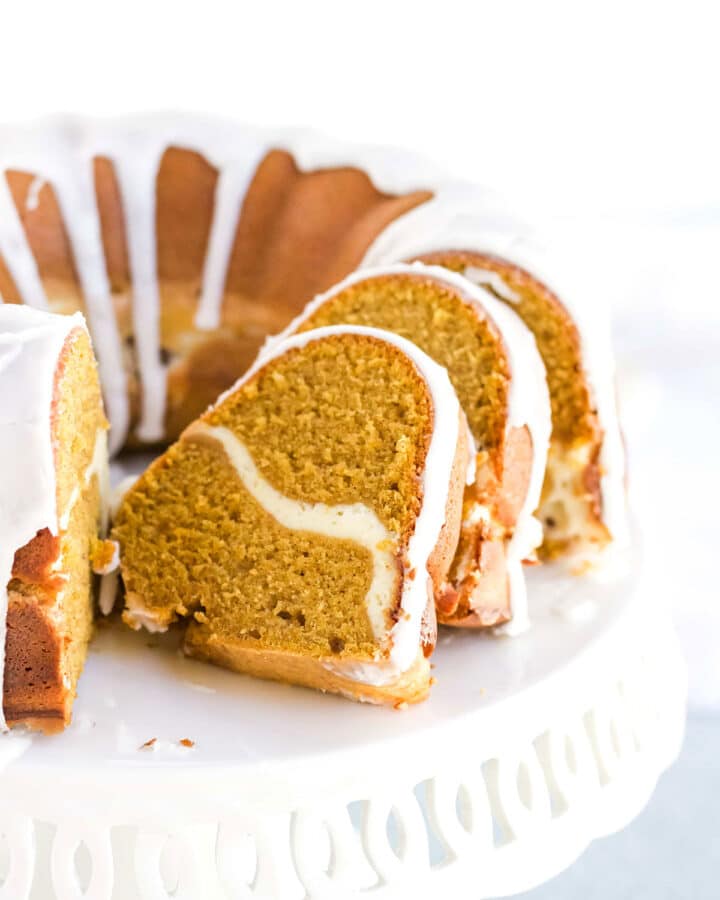 A pumpkin cream cheese pound cake sliced open on a white cake stand.