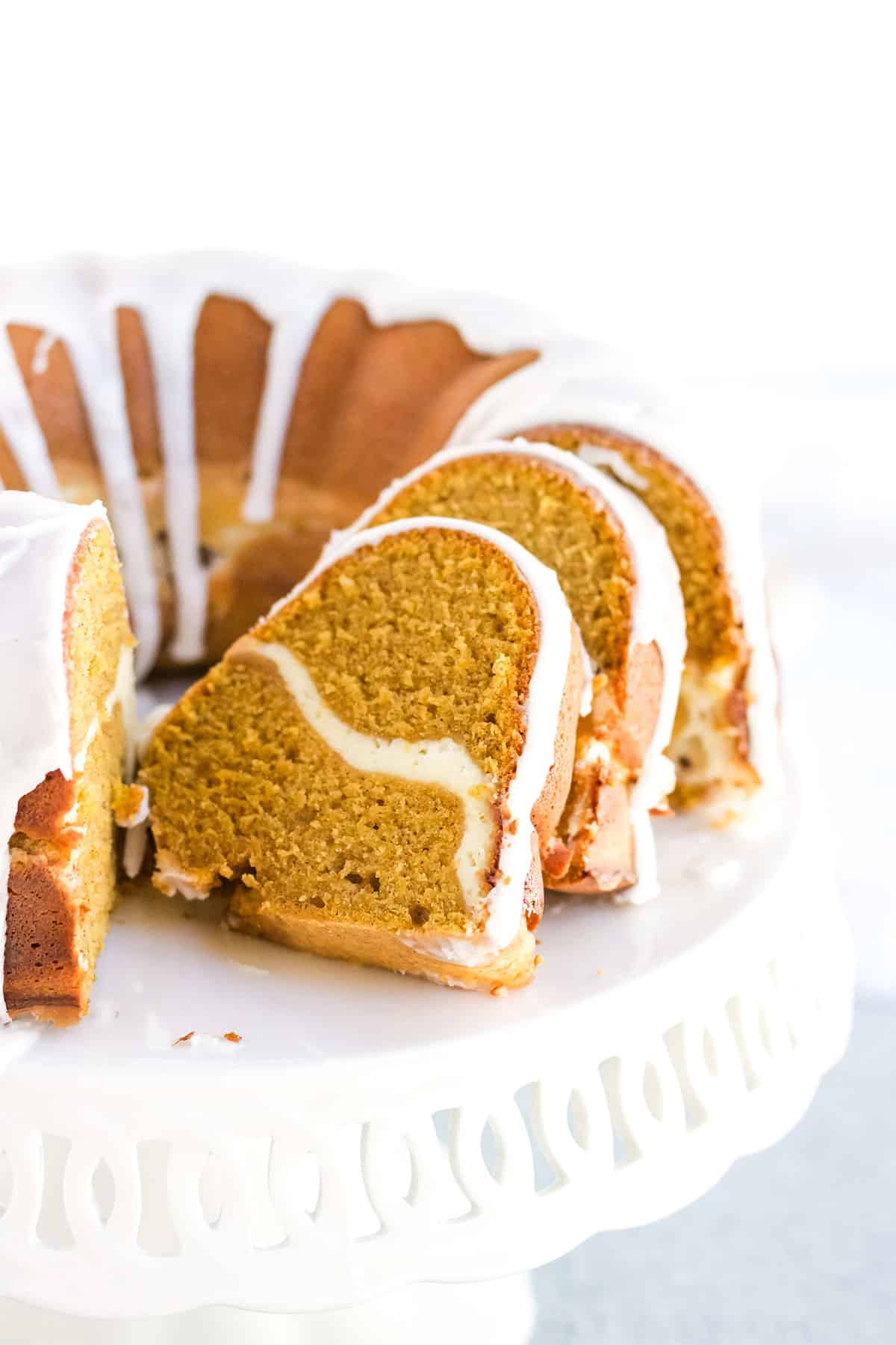 A pumpkin cream cheese pound cake sliced open on a white cake stand.