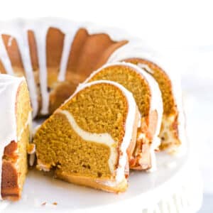 Pumpkin pound cake with cream cheese filling on a white cake stand.