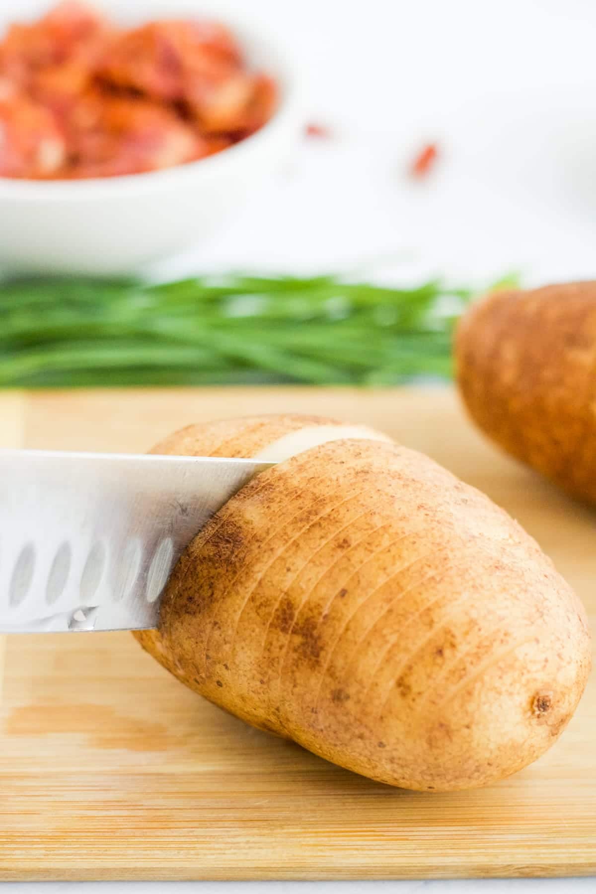 A potato being sliced on a cutting board to make Hasselback Potatoes. 