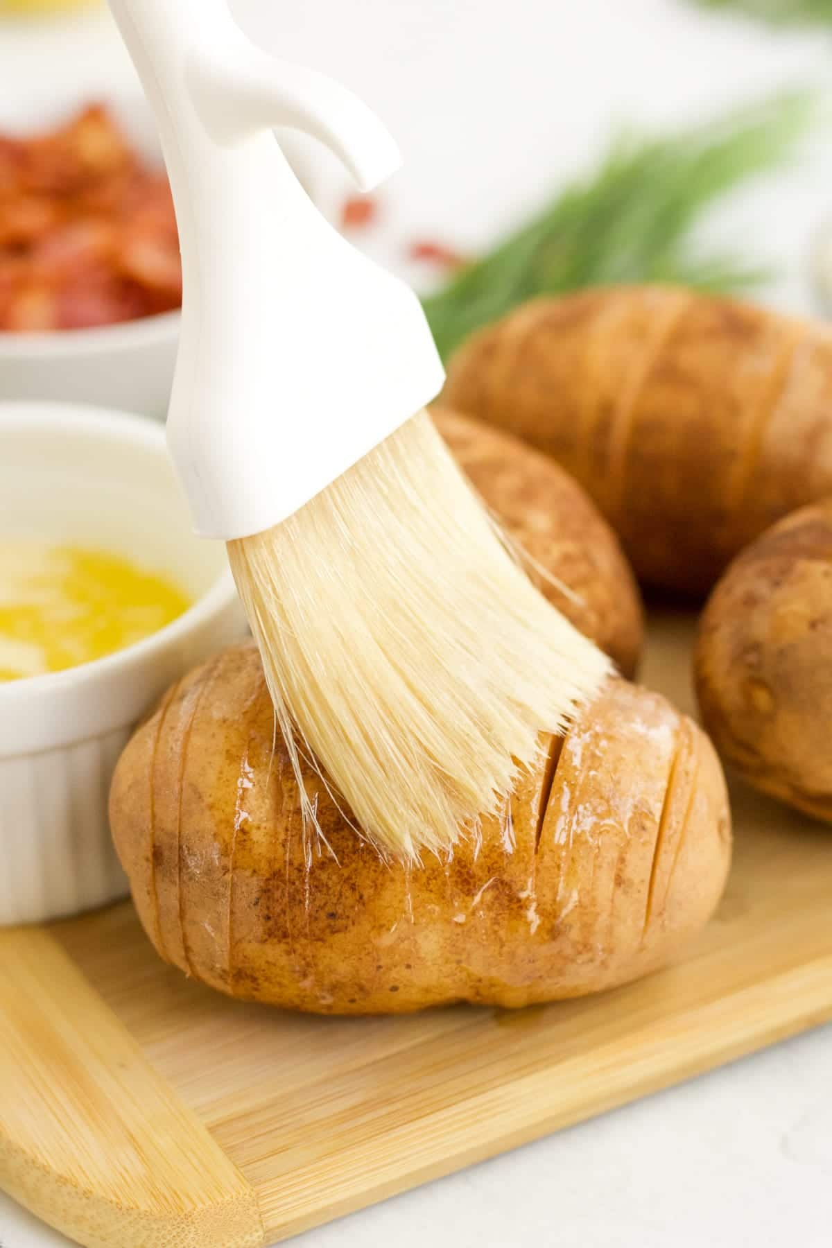 Olive oil being brushed on a potato before baking Hasselback Potatoes. 