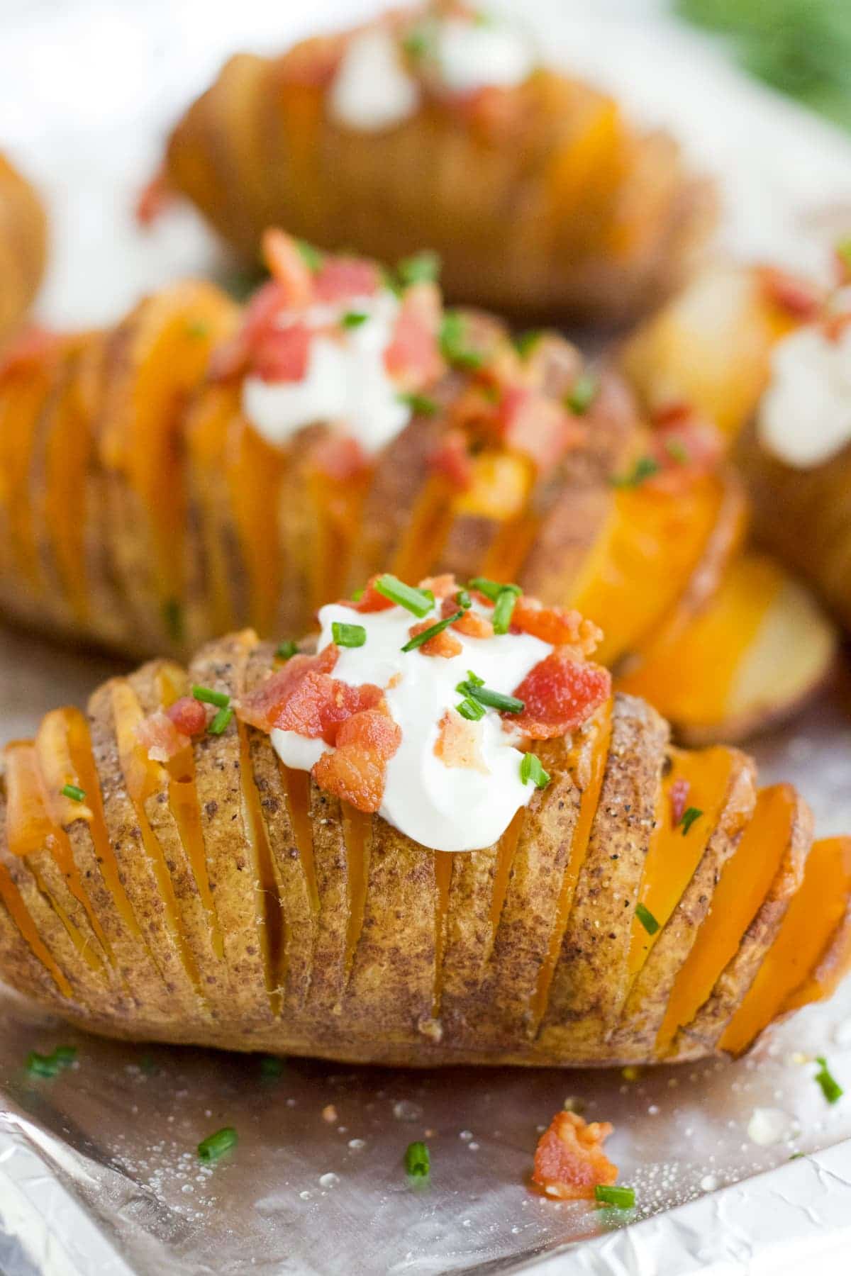 A close up image of a Hasselback potato with sour cream, bacon and chives. 