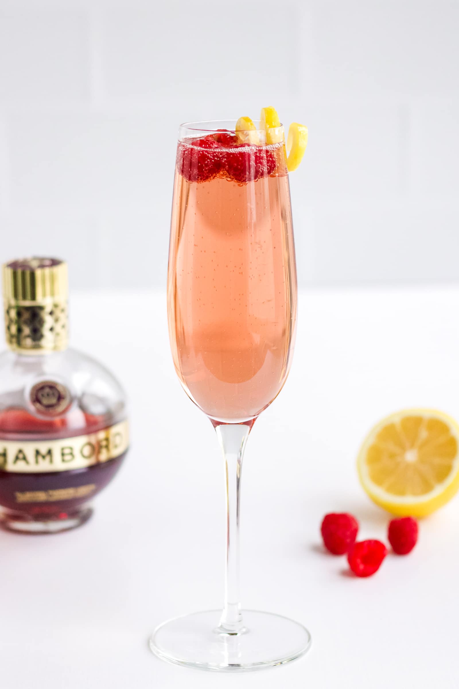 A glass of Chambord and Champagne with a lemon twist and three fresh raspberries on top. 