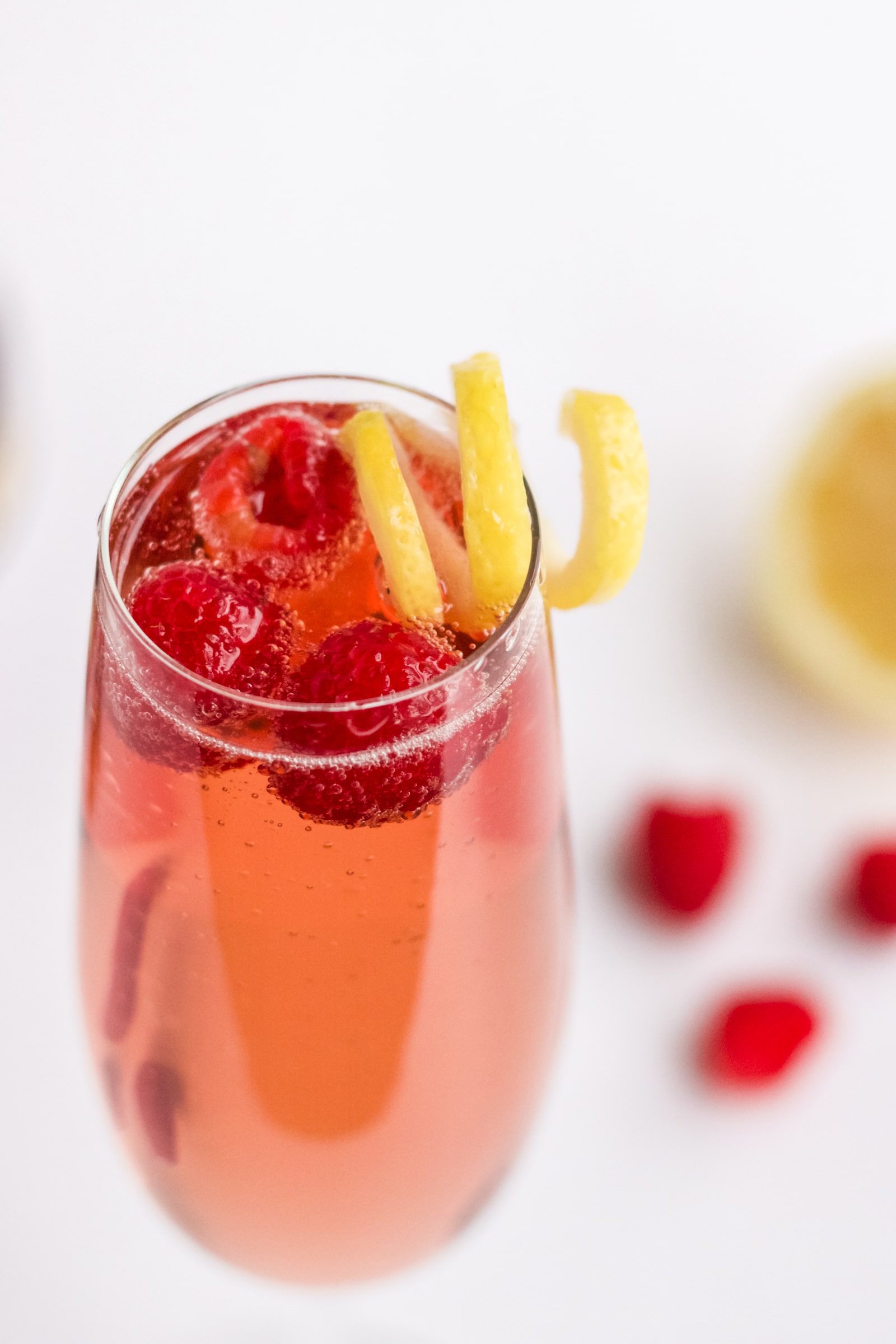 A close up image of chambord and champagne garnished with lemon twist and three raspberries. 