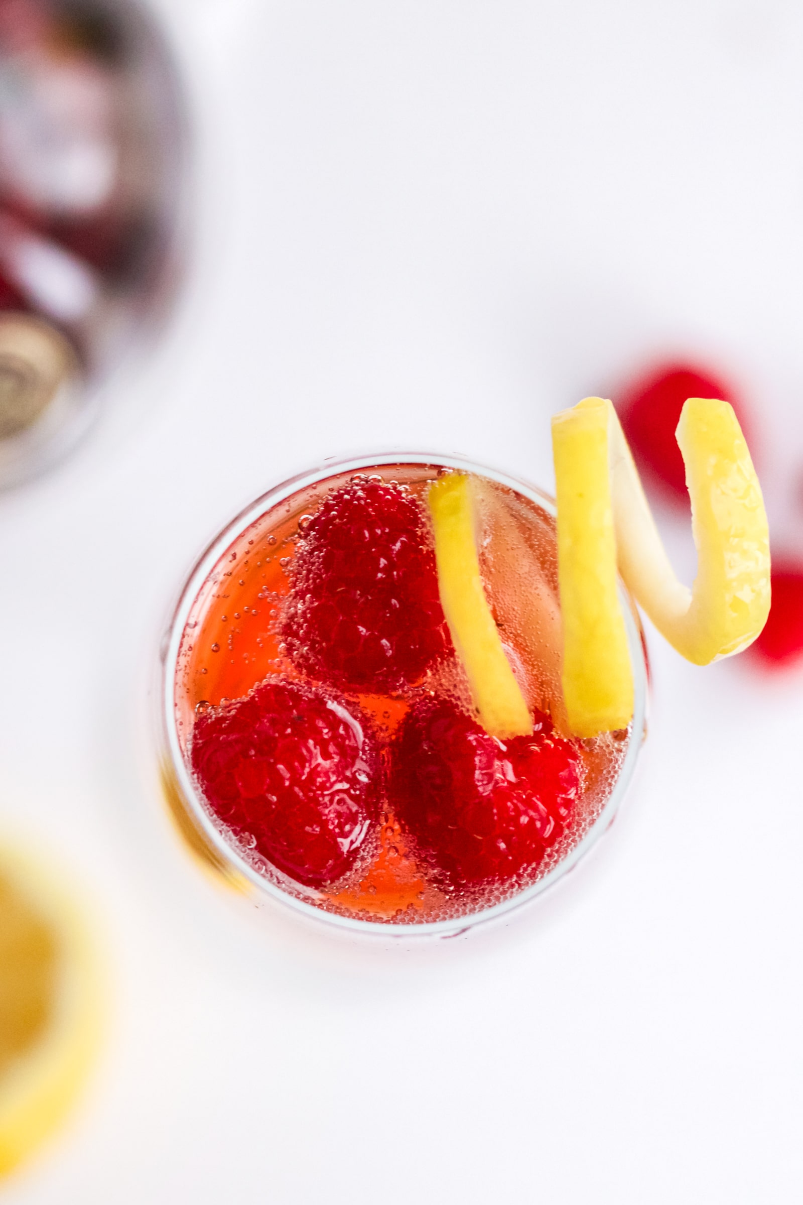 An overhead image of a French Mimosa with a lemon twist and three raspberries inside. 