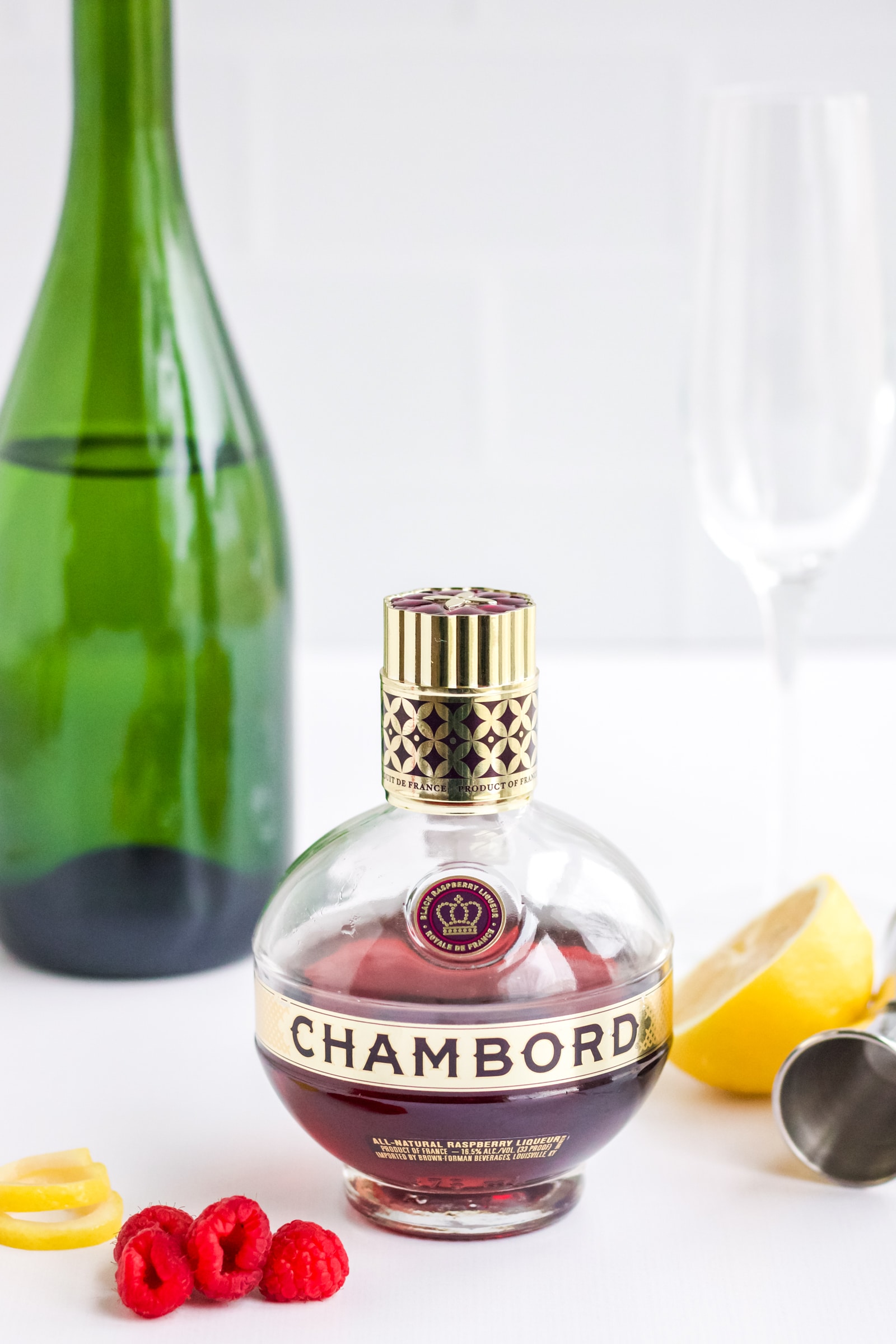 Ingredients for a Chambord and Champagne Cocktail - there is a bottle of chambord, a bottle of champagne and fresh lemon and raspberries. 