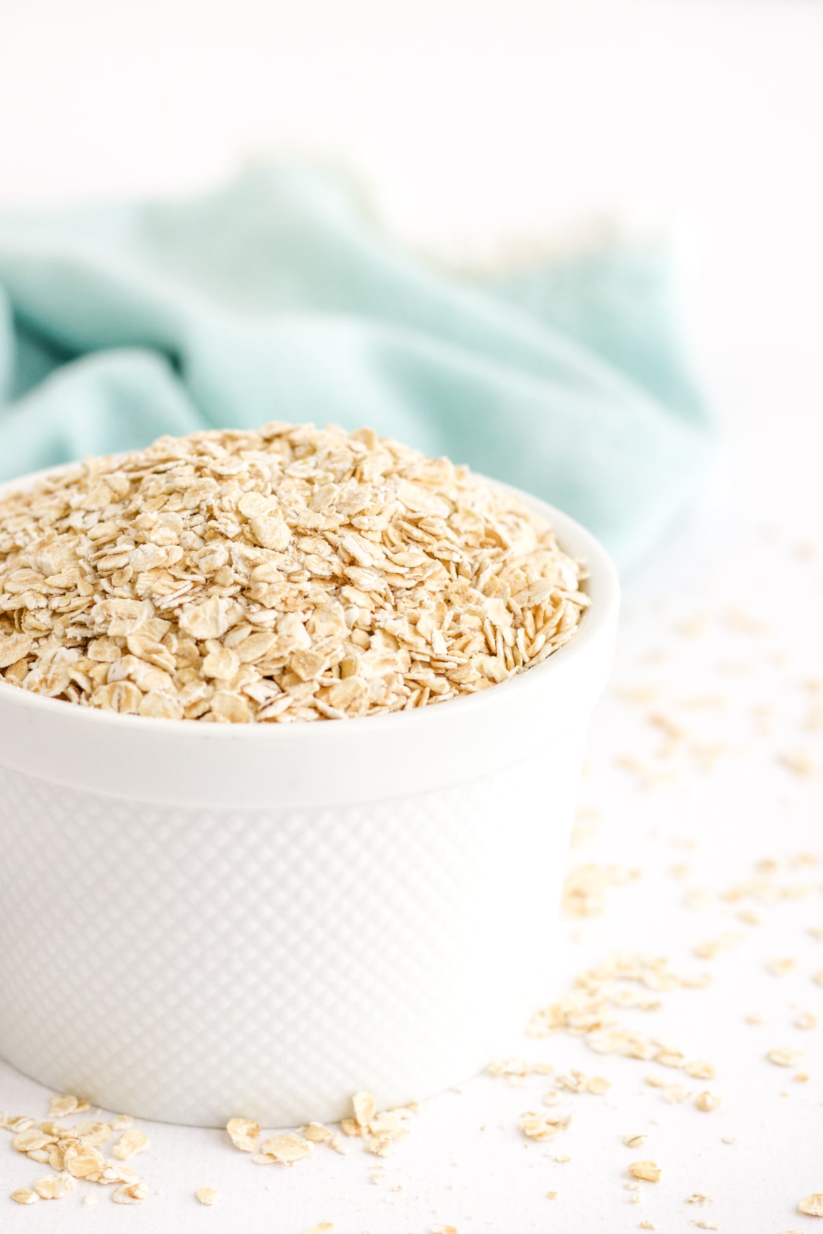 Rolled oats in a white bowl with a teal linen in the back to show how to make oat flour at home. 