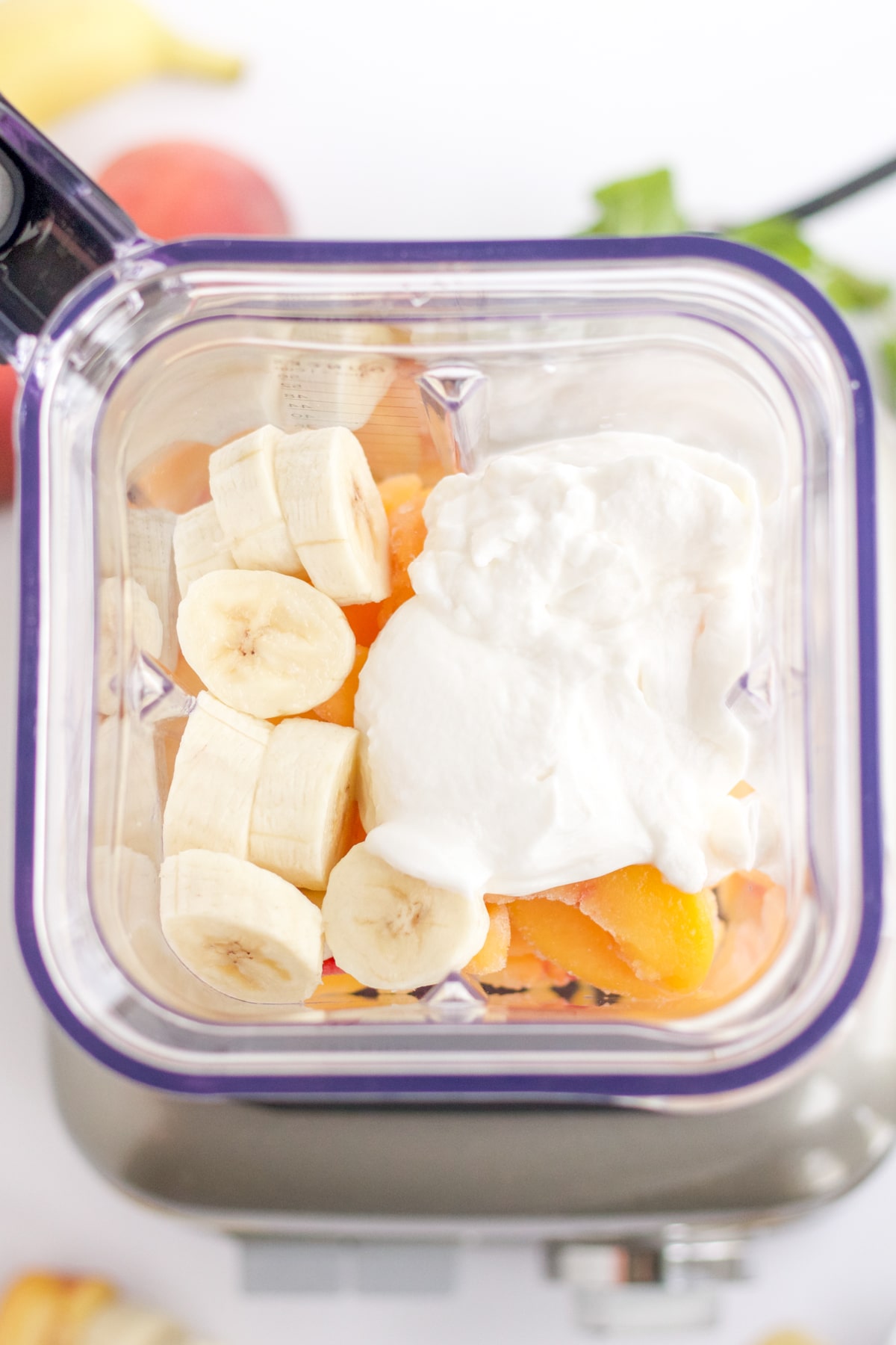 overhead shot of ingredients in a blender: bananas, yogurt and peaches