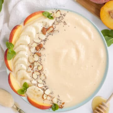 peach smoothie bowl with fresh fruit and nut toppings