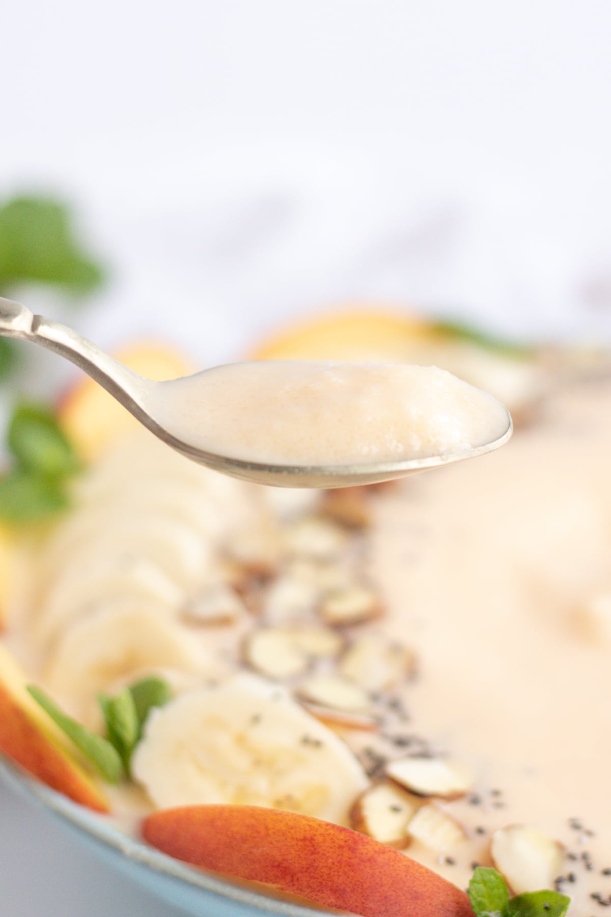 up close shot of spoon with peach smoothie and bowl in the background