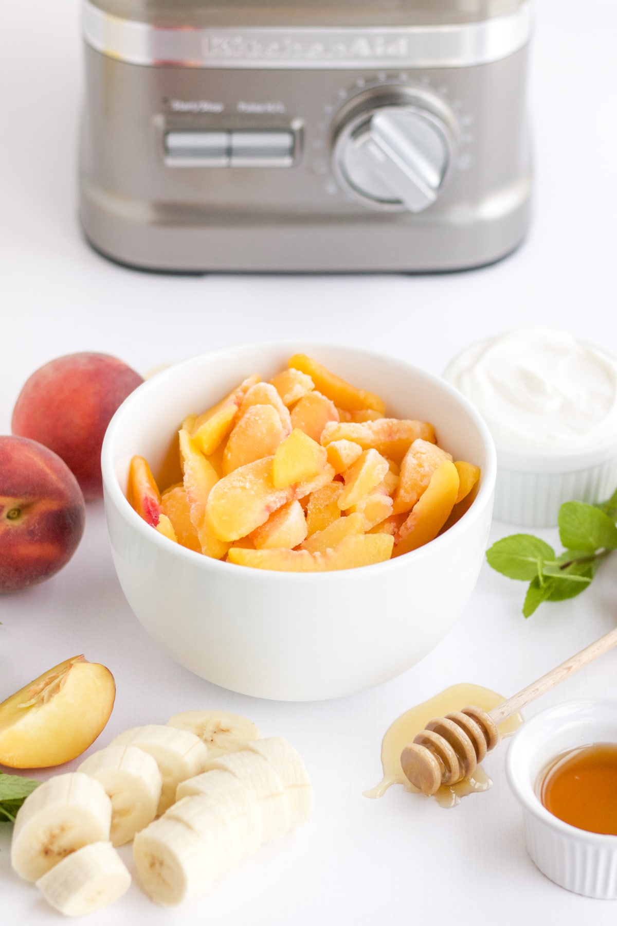 frozen peaches in a white bowl with a bananas, honey and yogurt