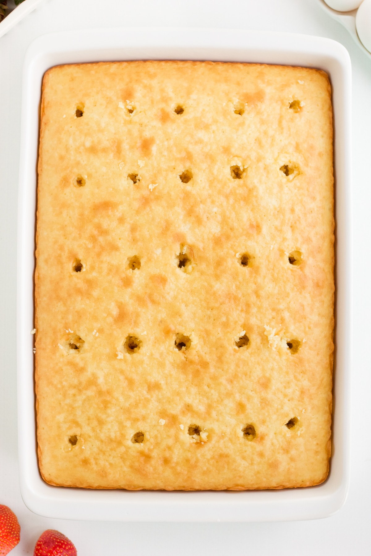 overhead shot of a cake in a white ceramic pan with holes poked across the top