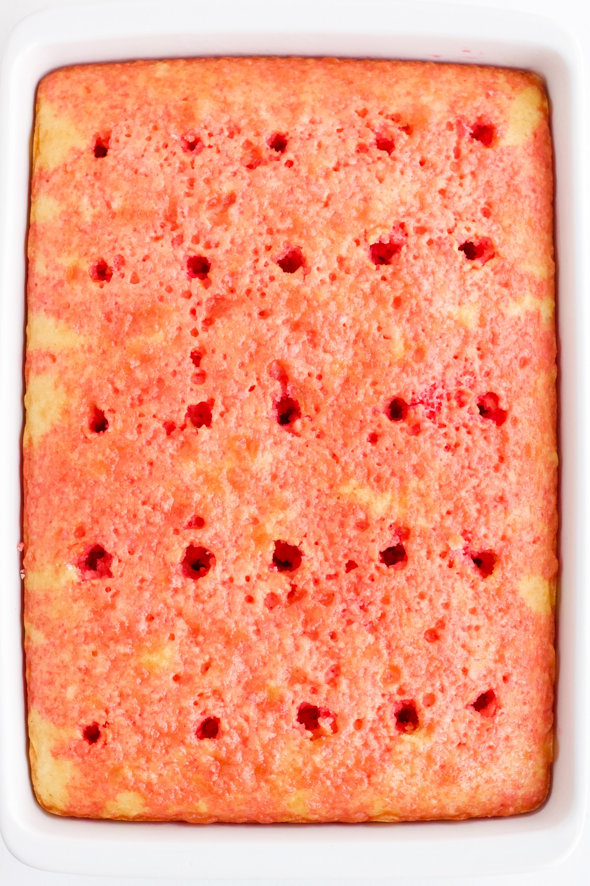 white cake with poke holes all over the top soaked in strawberry jello mixture