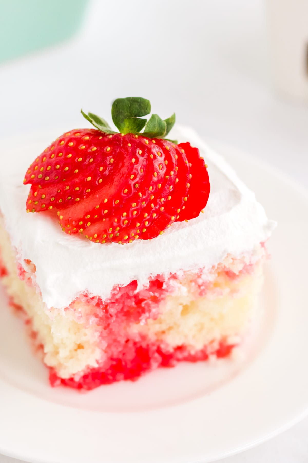 a square slice of white cake with strawberry filling on a white place topped with a strawberry