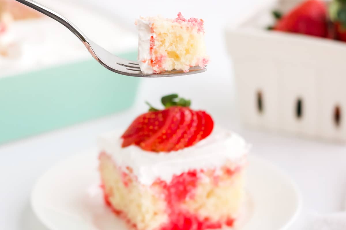 fork taking a bite from a slice of strawberry poke cake