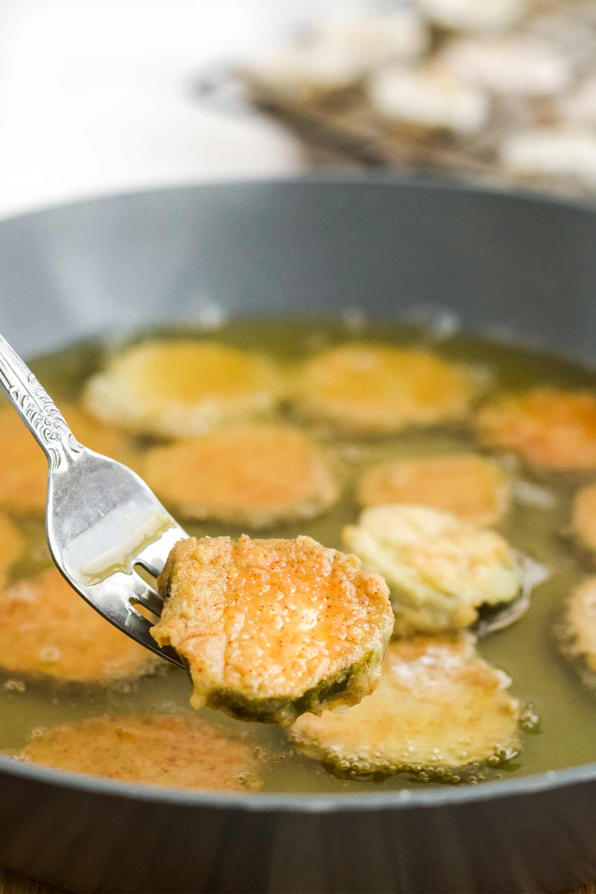 Frying the breaded pickle chips in a skillet.