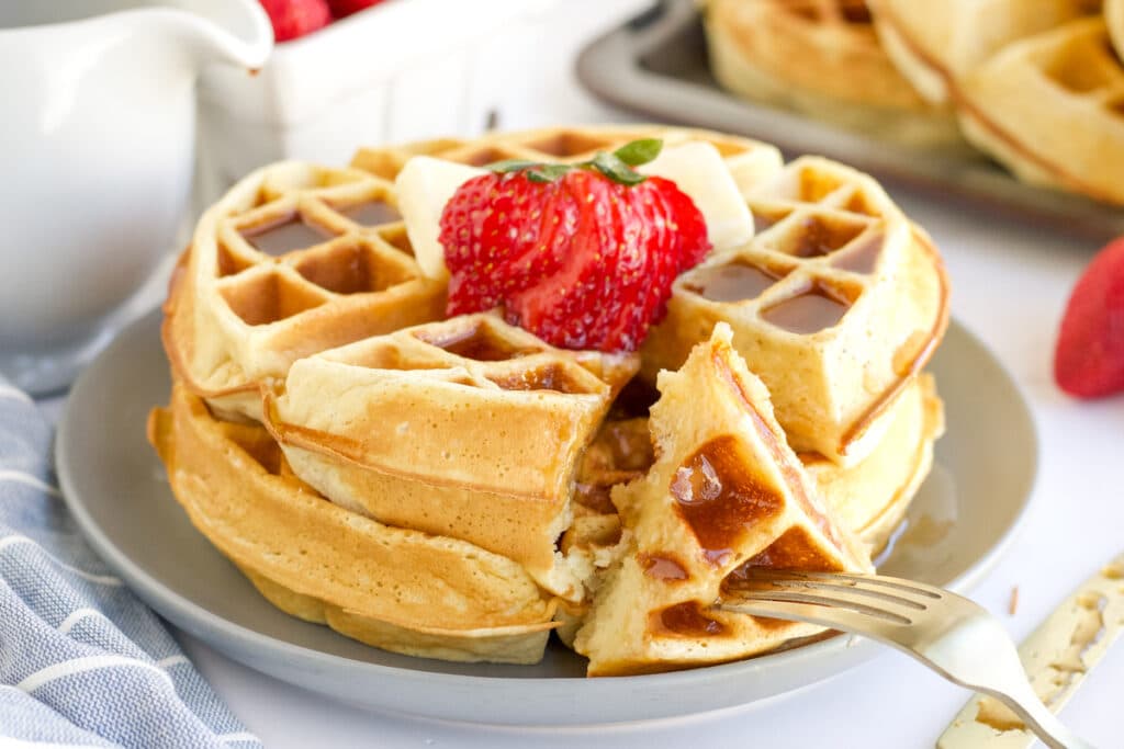 two belgian waffles stacked on a plate topped with strawberries