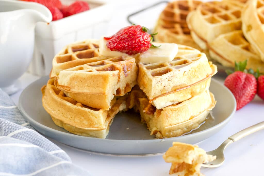 two belgian waffles stacked on a plate topped with strawberries