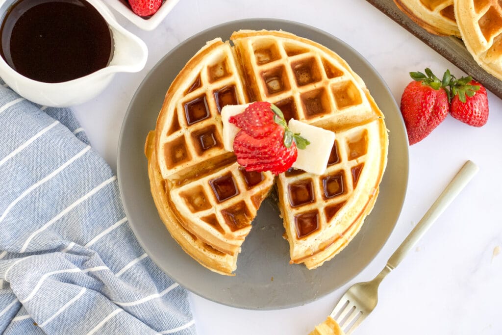 two belgian waffles stacked on a plate topped with strawberries