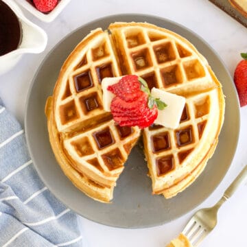 two belgian waffles stacked on a plate topped with strawberries