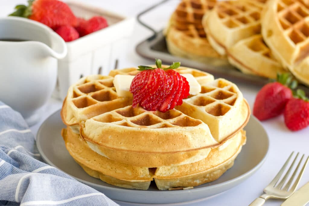 two belgian waffles stacked on a plate topped with strawberries