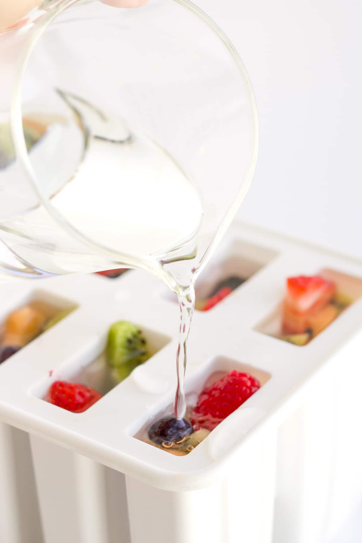 pouring clear juice into popsicle mold filled with fruit.