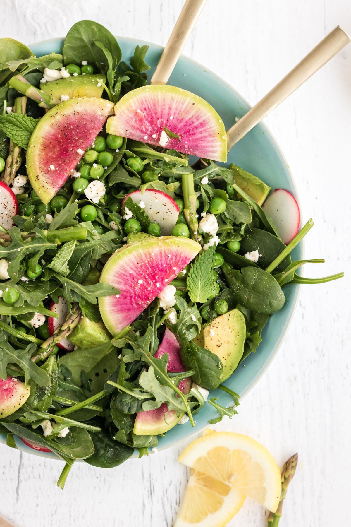 overhead shot of spring salad with pea, asparagus, and watermelon radish in blue bowl and serving spoons