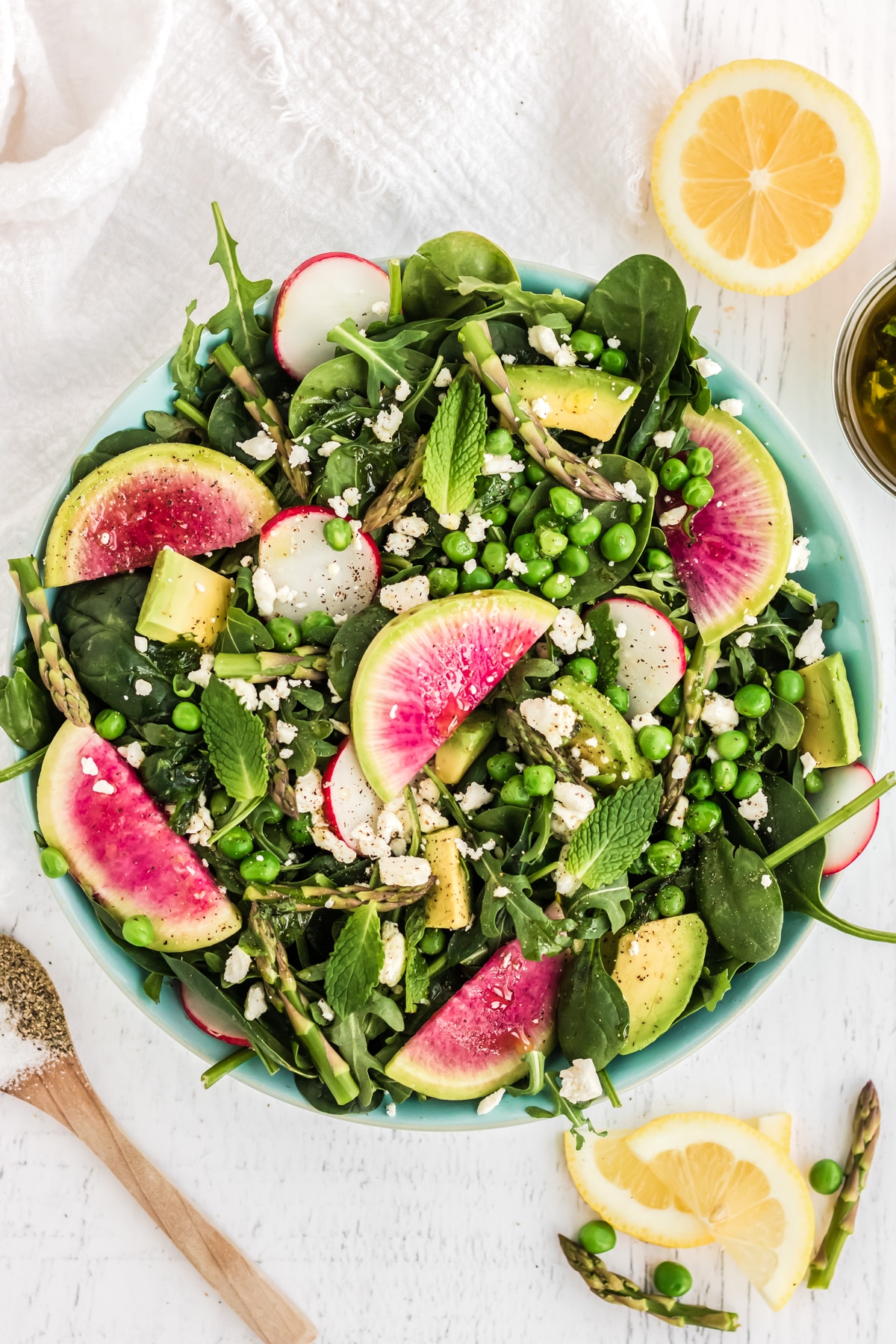 salad with peas, asparagus, watermelon radish, and feta cheese in a blue bowl on a white backgrop