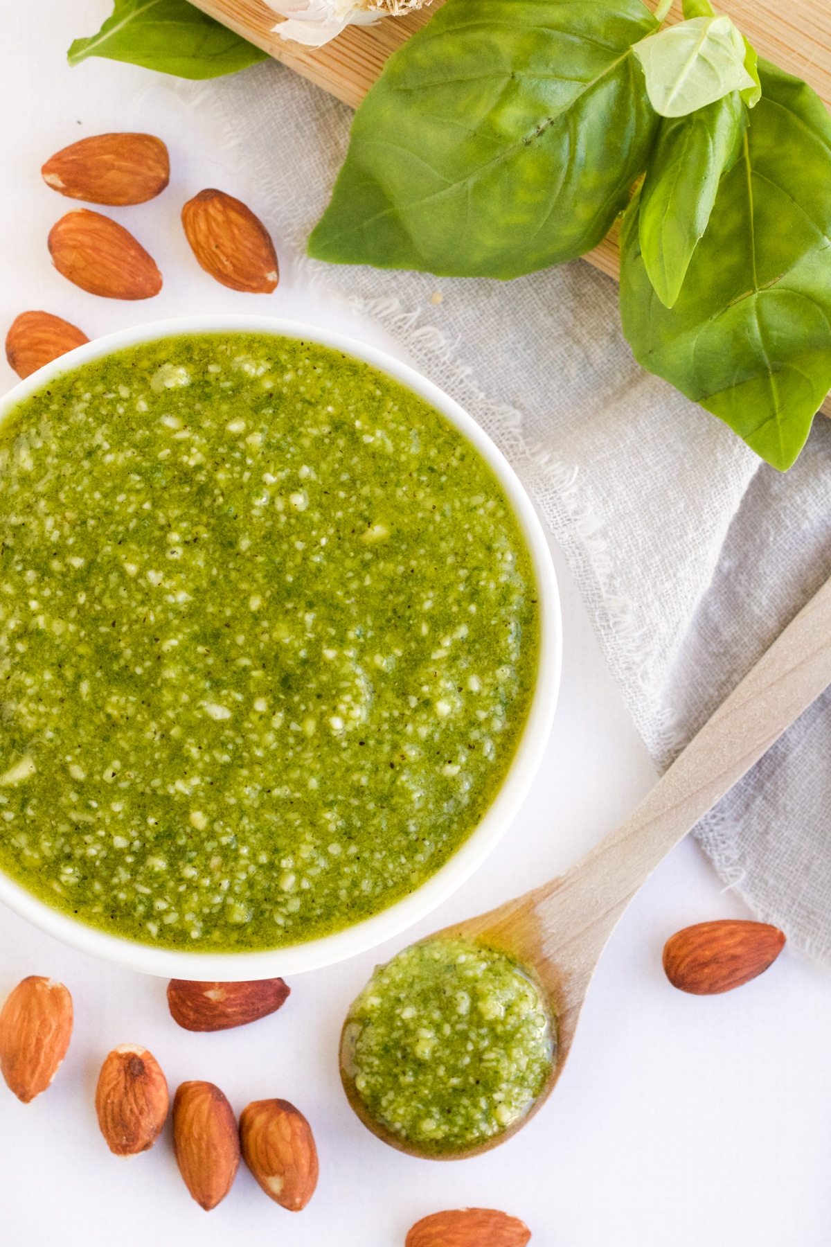 An overhead image of almond pesto sauce in a white bowl with a spoon and almonds around it.